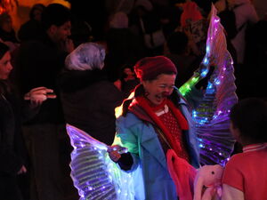 Im dunkeln. Frau mit farbig leuchtenden Flügeln geht durch die Menge der Besucher.