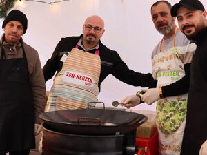 4 Männer mit Schürzen an einer großen Pfanne auf einer (Feuer?) Tonne