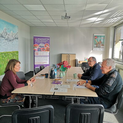 Konferenzraum, 1 Frau am Tisch, zwei Männer sitzen ihr gegenüber.