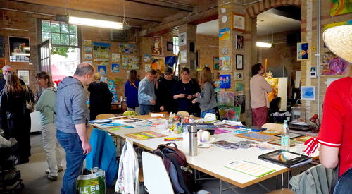 Atelier. Großer Raum mit Bildern an den Wenden. Menschen schauen sich die Kunst an.