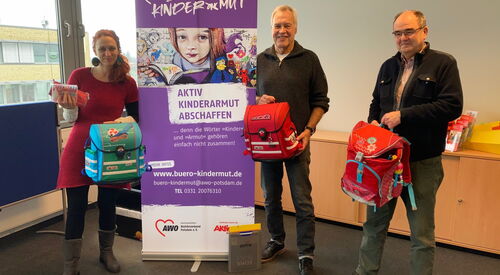 Spendenausgabe im Büro Kindermut, 3 Personen mit Kinderrucksäcken