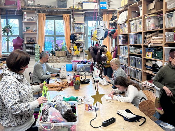 Frau links vorne kramt in einer kiste mit Stoffen. Rechts außen große gefüllte Regale.