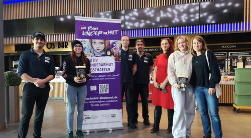 Gruppenfoto mit lila Roll-Up Banner vom AWO Büro Kindermut. 3 Angestellte vom Kino und 4 Frauen lächeln in die Kamera. Zwei der Frauen haben Popcorn in den Händen.