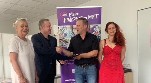 4 Personen vor einem Roll-Up des Büro Kindermut. 2 Frauen außen, innen schütteln sich die Männer die Hand.