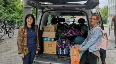 Zwei Frauen am Heck eines beladenen Transporters mit offener Heckklappe.