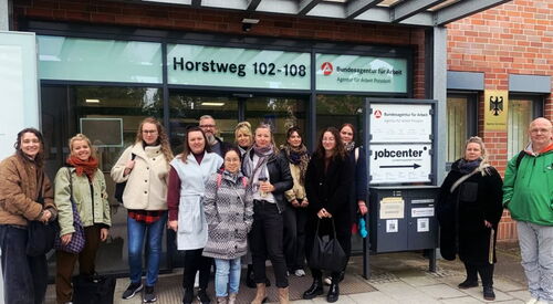Gruppenbild: 13 Menschen vor dem Eingang zur Bundesagentur für Arbeit.