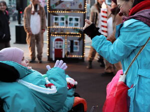 Kind im Rollstuhl, warm eingepackt, sieht zur Clownin. Diese steht neben ihm und lächelt.