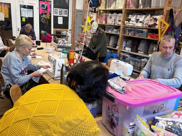 Langer Tisch mit Nähmaterial und Nähmaschinen, ein Mann und Frauen beschäftigt.