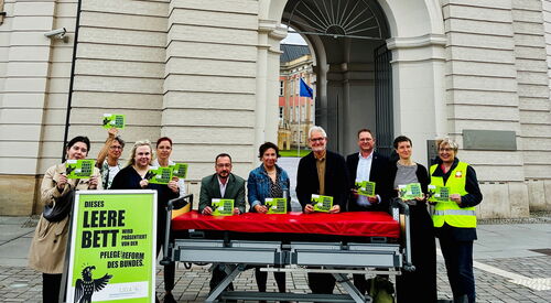vor dem Fortuna Portal. Ein leeres Pflegebett, ein großes grünes Schild und 10 Menschen mit grünen Karten, mit Aufschrift.