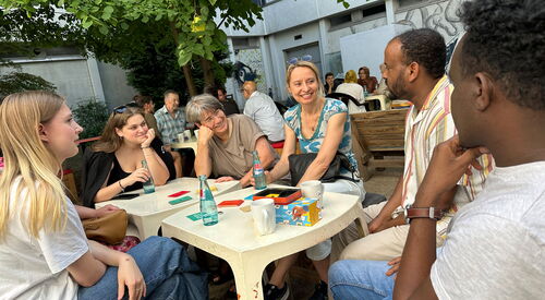 Gesellige Beisammensein, an Picknicktischen. Menschen mit verschiedenen Hautfarben mit Getränken an Tischen.