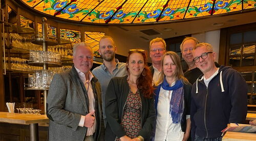 Gruppenfoto: 5 Männer und mittig zwei Frauen. In einen schicken Raum mit gelben Fließen und einer hübsch verzierten Decke.