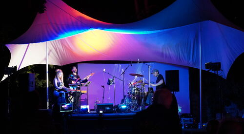 Konzert am Abend im Dunkeln. Bühne mit drei Musikern, Keyboard, Gitarre Schlagzeug.