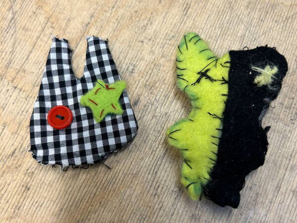 Zwei kleine, genähte Figuren: links eine karierte Form, rechts eine grün-schwarze Figur, auf hellem Untergrund.