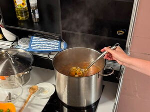 In einer Küche, Topf mit Suppe auf dem Herd. Person rührt um.