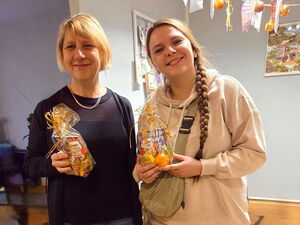 Zwei Frauen stehen in einem Raum und halten jede eine Geschenktüte in der Hand und lächeln.