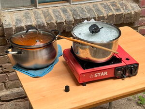 Tisch draußen. Ein Topf mit Essen auf einem Handtusch und ein Topf auf mobiler Heizplatte. Roter Campingkocher.