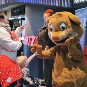 Das braune Maskottchen klatsch mit einen Kleinkind im Kinderwagen ab. Vor Kino 2.