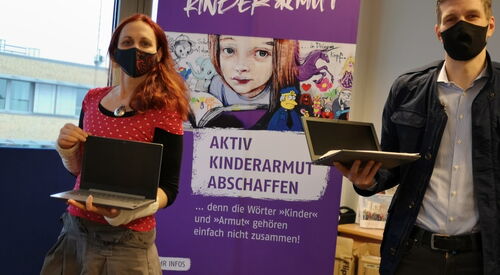 2 Personen vorm Plakat vom Büro Kindermut mit Laptops in den Händen