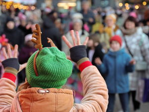 Von hinten: Mensch mit grüner Mütze und Rentier-Kostüm streckt Arne aus und winkt.   Zuschauer unscharf im Hintergrund.