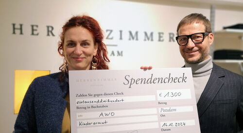 Eine Frau und ein Mann halten einen Spendenscheck in die Kamera.
