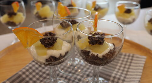 Mehrere Gläser mit Apfelkompott und Weizengrieß Garnierung am Glasrand mit Orangenstücken auf einem gedeckten Tisch.