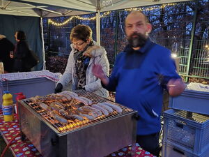 Mann am Bratwurstgrill. Daneben eine Frau die sich um die Brötchen kümmert.