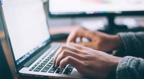 Eine Person arbeitet an einem Laptop. Handy auf Tastatur. Von der Seite fotografiert.
