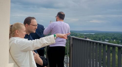 Menschen schauen von einer Aussichtsturm über Potsdam. Blonde Frau mit weißer Jacke streckt Arm aus und zeigt mit Finger nach rechts. Neben ihr ein Mann der in die gezeigte Richtung schaut.