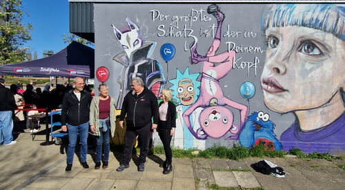 Gruppenbild. 4 Personen, 2 Männer, 2 Frauen vor eine bunten mit Figuren bemalten Graffiti Wand.