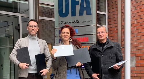 2 Männer, eine frau mit roten Haaren in der Mitte. Sie halten Laptops / Notebooks in der Hand. Vor einen ein Rollwagen mit weiten Geräten.