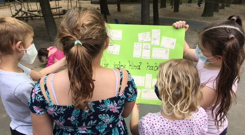 1 Erwachsener und 3 Kinder halten ein Plakat mit Kinderzeichnungen in den Händen