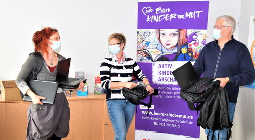 3 Personen vor einem Plakat des Büro Kindermutes mit Laptops in der Hand
