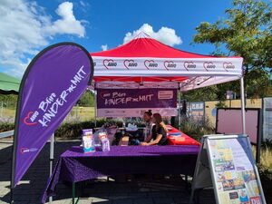 Roter AWO Pavillon mit lila Tischdecken auf den Tischen mit Info-Material. Links eine Lila Beachflag von AWO Büro Kindermut.