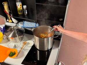 In einer Küche, Topf mit Suppe auf dem Herd. Person rührt um.