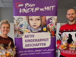 In der Mitte das lila Roll-Up vom Büro Kindermut. Links eine Frau und rechts ein Mann mit Geschenktütchen in den Händen.