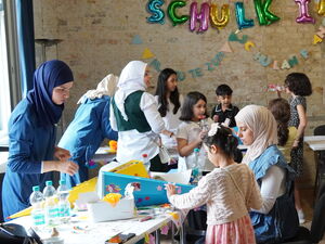 Kinder und Mütter bekleben / gestalten Zuckertüten. Großer Raum mit Tischen und bunt für die zukünftigen Schulkinder geschmückt.