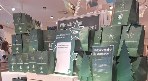 Regal in einer Drogerie. Mit vielen dunkelgrünen Adventstüten. Weihnachtlich dekoriert mit Sternen und Tannenbäumen.