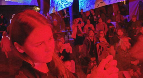 Besuchende des Festes. Publikum in rotes Licht getaucht. Es ist dunkel.