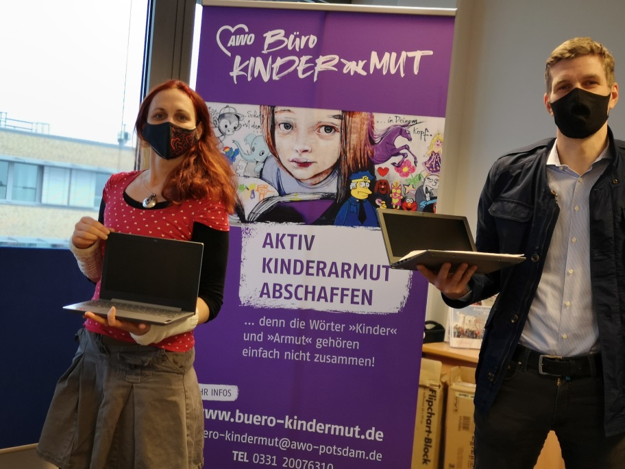 2 Personen vorm Plakat vom Büro Kindermut mit Laptops in den Händen