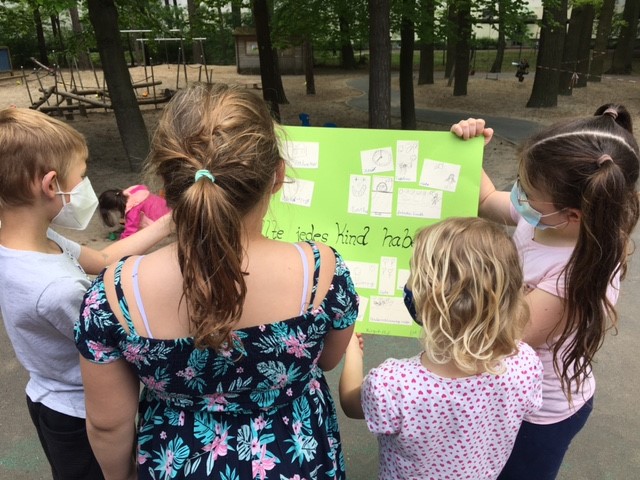 1 Erwachsener und 3 Kinder halten ein Plakat mit Kinderzeichnungen in den Händen