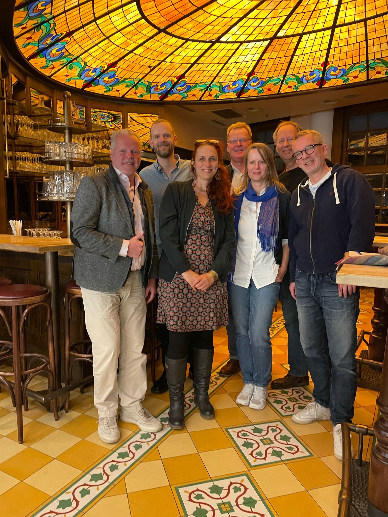 Gruppenfoto: 5 Männer und mittig zwei Frauen. In einen schicken Raum mit gelben Fließen und einer hübsch verzierten Decke.