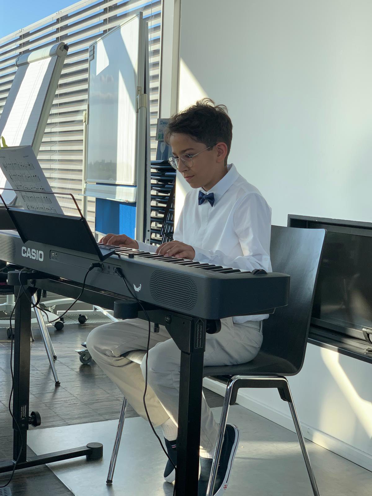 Junge sitzt am Keyboard. Er trägt ein weißes Hamd und eine schwarze Fliege.