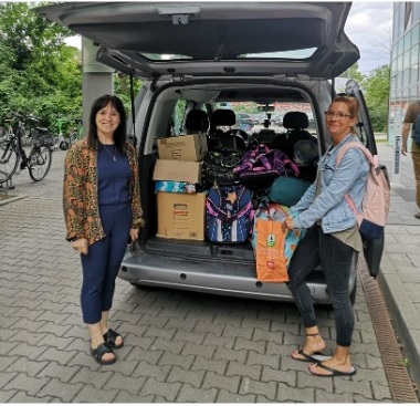 Zwei Frauen am Heck eines beladenen Transporters mit offener Heckklappe.