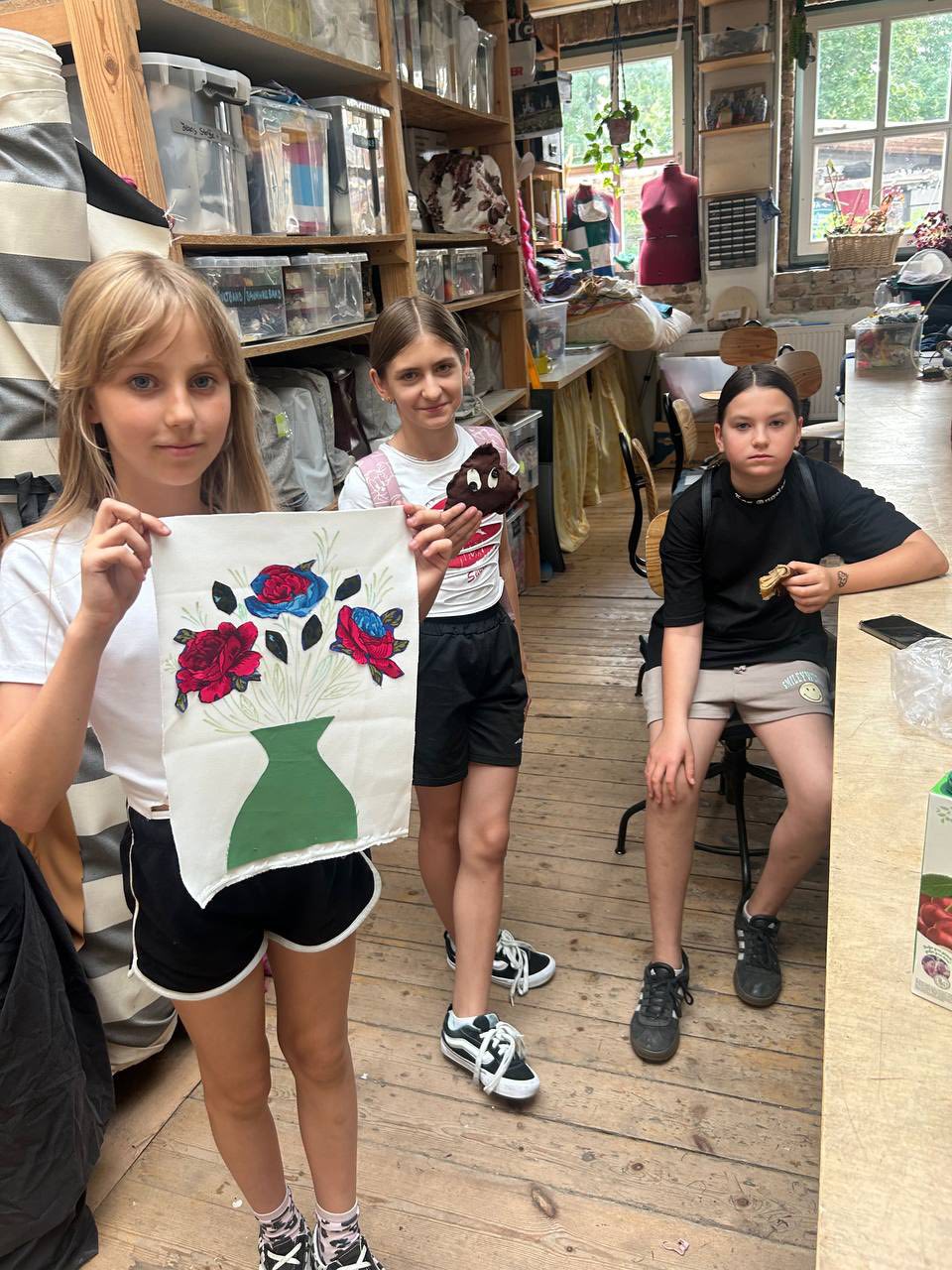 Drei Mädchen zeigen ihre genähten Werke.