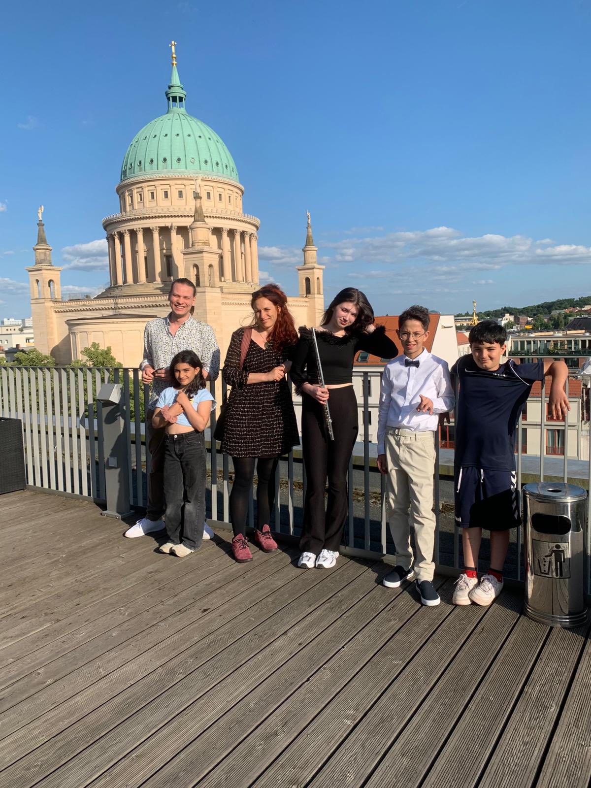 Auf einer sonnigen Dachterrasse stehen zwei Erwachsene und vie Kinder / Jugendlich an der Brüstung und lächeln in die Kamera.